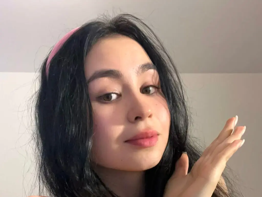 Close-up portrait of a young woman with long dark hair and a pink headband in soft indoor lighting.