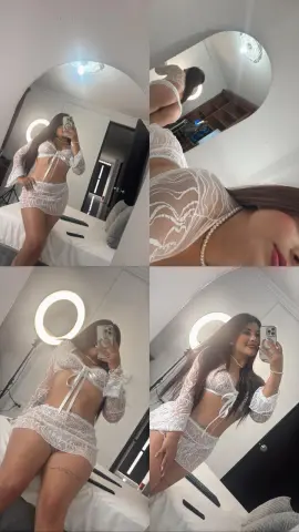 Young woman in a white lace lingerie set posing in a bright bedroom with a ring light.