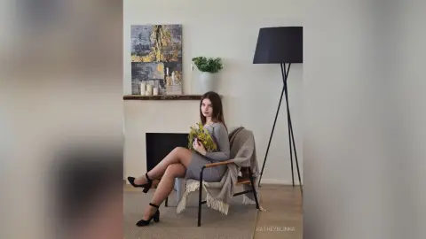 Elegant woman in a grey dress sitting in a modern living room with minimalist decor and warm lighting.