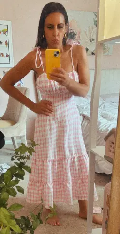 Woman in a pink gingham sundress posing in a bright bedroom for a summer fashion look.