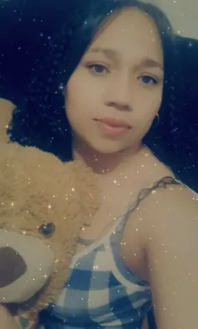 Young woman in a blue checkered tank top hugging a brown teddy bear in a cozy, sparkling setting.