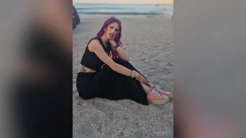 Red-haired woman in a black summer outfit sitting on a sandy beach at sunset with a relaxed mood.