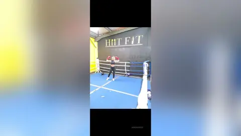 Athletic woman in black workout gear training in a modern boxing gym with blue ring mats.