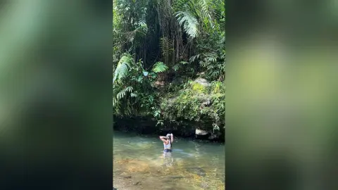 Young woman in a white bikini relaxing in a serene tropical jungle river surrounded by lush green foliage.