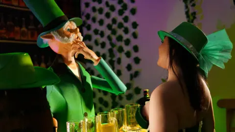 Woman in green costume interacting with a leprechaun figure at a festive St. Patrick's Day themed party.