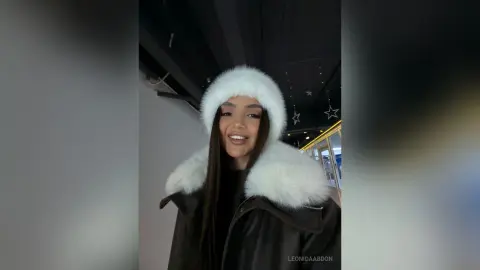 LeonidaAbdon wearing a white furry hood and a black leather jacket, looking at the camera with long dark hair.