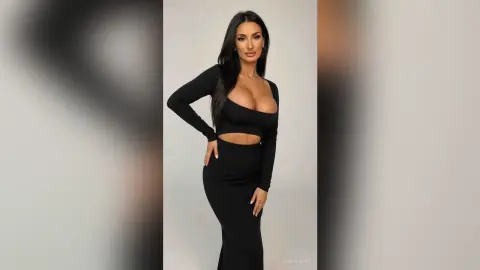 AnnaKarev poses in a tight black long-sleeve crop top and matching skirt, showing off her large breasts and long dark hair.