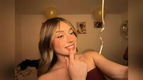 Smiling young woman in a maroon top celebrating at a party with gold balloons in a warm indoor setting.