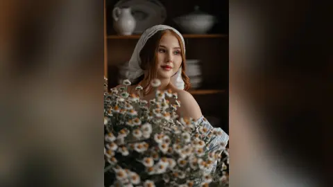 Dreamy portrait of a young woman in a white lace outfit holding a bouquet of daisies in a rustic indoor setting.
