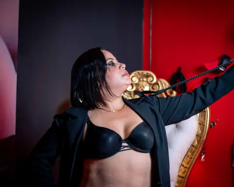 Confident woman in a black blazer and bra posing against a red and black background.
