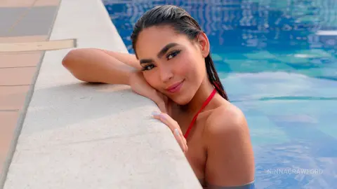 Smiling young woman in a red bikini relaxing by a bright blue swimming pool on a sunny summer day.