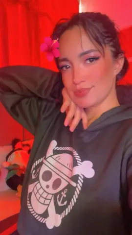 Young woman in a dark graphic hoodie smiling in warm red lighting.