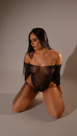 Elegant woman in a black sheer sparkly bodysuit posing in a studio setting with moody lighting.