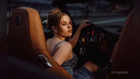 StelaBrown sits in the driver's seat of a car, looking back over her shoulder with her blonde hair in a bun.
