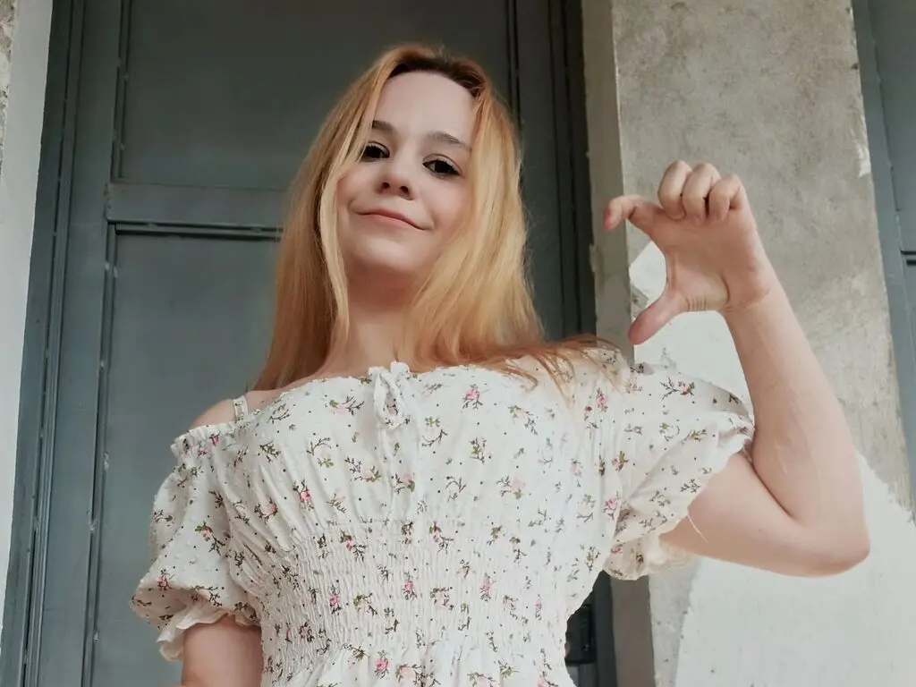 Smiling young woman in a white floral summer dress posing outdoors against a rustic grey door.