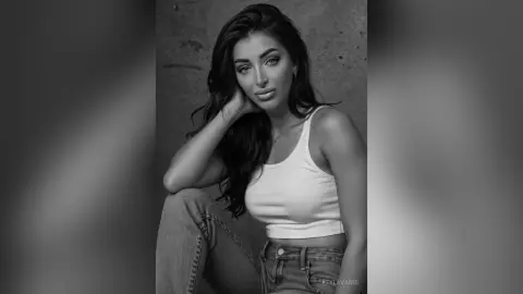 Elegant woman in a white ribbed tank top posing against a textured wall in a moody black and white portrait.