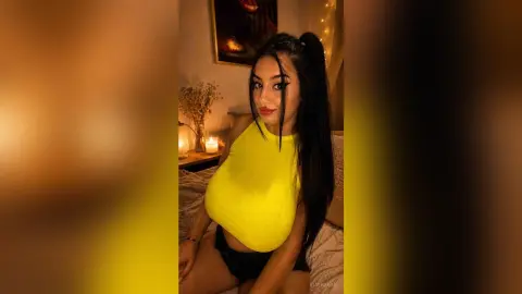 Young woman in a yellow halter top sitting in a cozy, dimly lit room with warm candlelight.