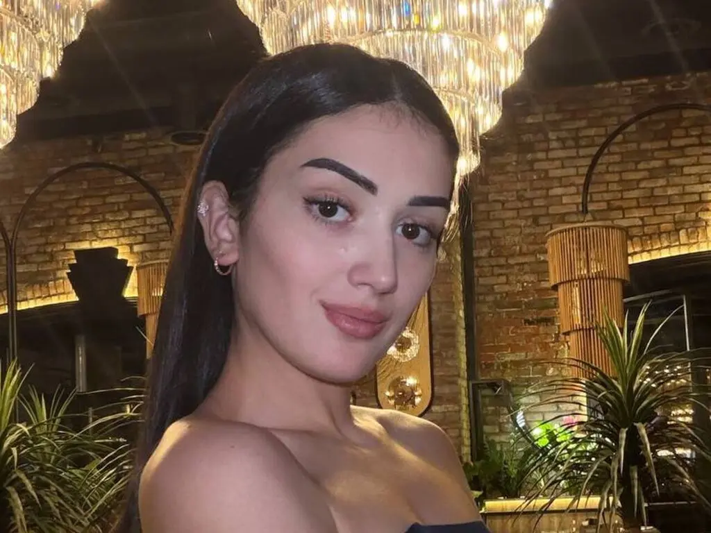 Young woman with long dark hair posing in a warm, dimly lit upscale restaurant setting.