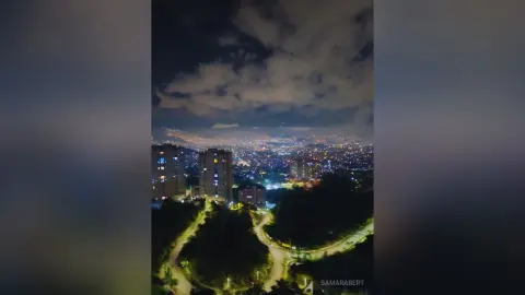 SamaraBert overlooking a bright, lit-up city skyline at night under a cloudy dark sky.
