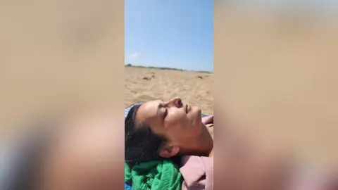 MichaelaBelle lies on her back on a beach, looking up toward the sky with her eyes closed.
