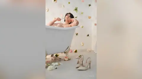 Elegant woman relaxing in a white vintage bathtub surrounded by pink roses in a dreamy, romantic setting.