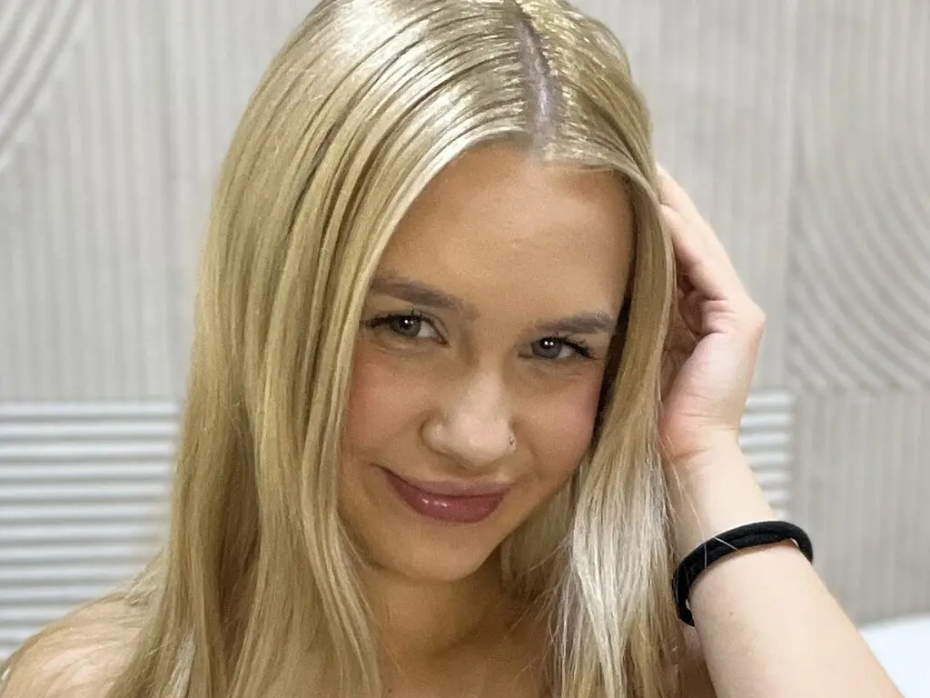 Smiling blonde woman with long hair posing in a bright, modern indoor setting.