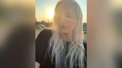 Blonde woman in a black shirt enjoying golden hour sunlight in an outdoor setting.