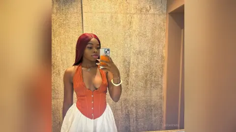 BecaSpark poses for a mirror selfie wearing an orange corset top and a white skirt.