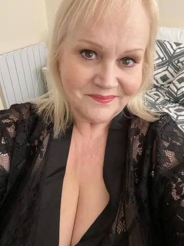 Busty_Madeline smiles while wearing a black lace robe that shows off her cleavage, posing in a bedroom setting.