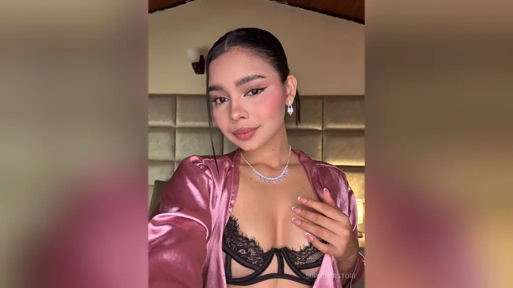 SophiaPastori โ SophiaPastori wears a pink satin robe and black lace bra while posing in a bedroom.