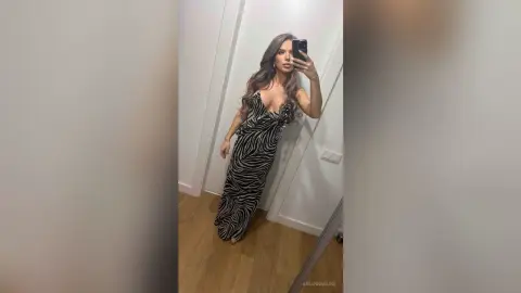 Woman in a black and white zebra print maxi dress taking a mirror selfie in a modern minimalist room.