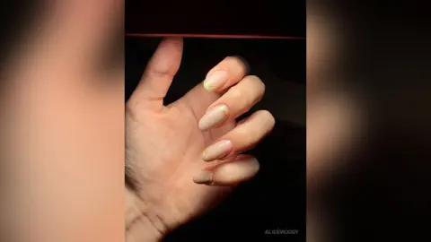 Close-up of a hand with elegant nude almond-shaped manicured nails against a dark moody background.