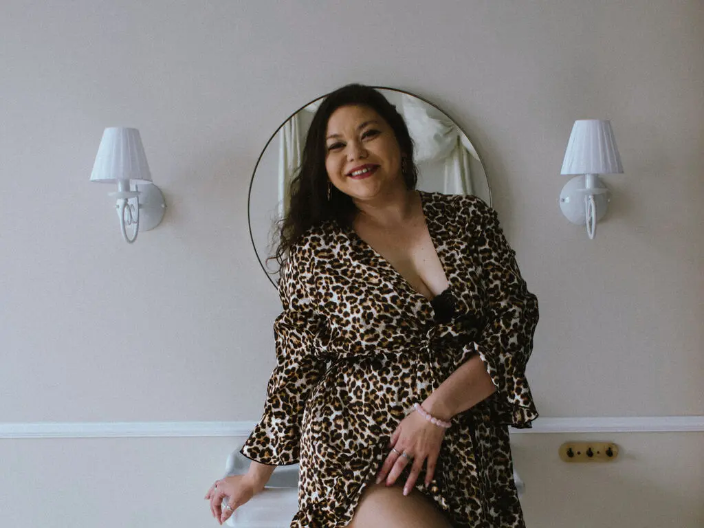 Smiling woman in a leopard print wrap dress posing in a bright, minimalist room.