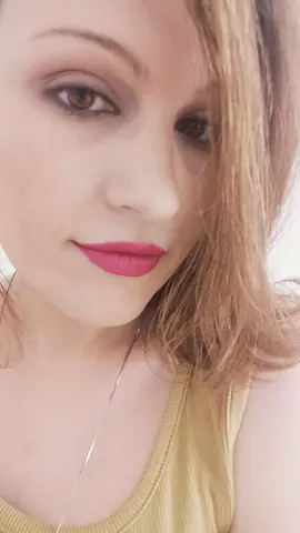 PEARLLxo wearing a yellow ribbed tank top with bright pink lipstick and long light brown hair.