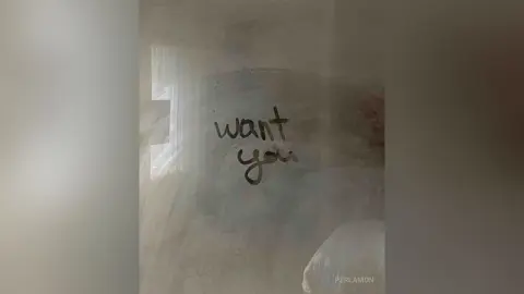 Handwritten black text reading 'want you' on a textured, moody grey wall in a minimalist setting.