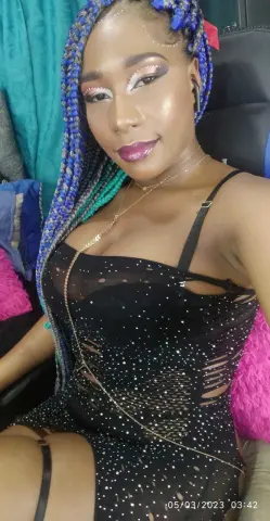 Glamorous woman with blue braids in a black sequin cutout dress posing in a cozy indoor setting.