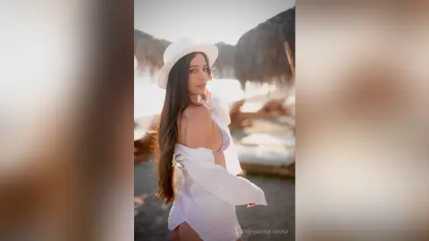 Young woman in a white sun hat and breezy white shirt relaxing on a sunny tropical beach.