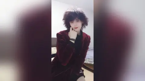 Young woman with dark wavy hair wearing a luxurious red velvet blazer in a cozy indoor setting.