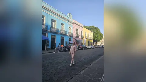Stylish woman in beige trousers standing on a cobblestone street by colorful historic buildings at sunset.