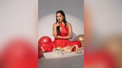 Elegant woman in a red satin dress sitting by a birthday cake and balloons in a celebratory mood.