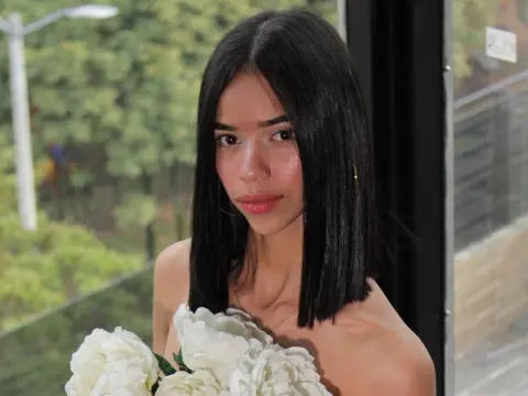 Young woman with straight dark hair holding white peonies on a balcony during a soft summer afternoon.