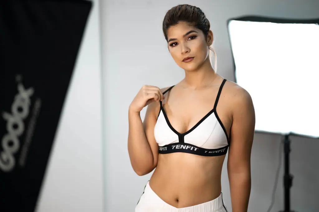 ScarlettZhen — Confident woman in white sports bra posing in a professional photography studio with soft lighting.