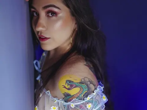 Woman with long dark hair and snake tattoo wearing a white floral blouse in moody blue lighting.