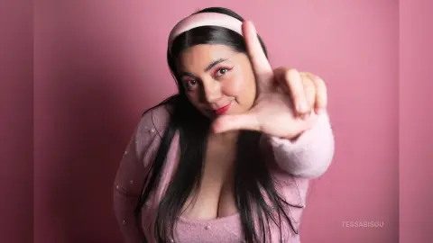 Smiling woman in a pink sweater and headband posing against a soft pink background for a dreamy aesthetic.