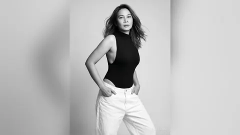 MilaSwan — MilaSwan poses in a black halter bodysuit and white pants against a plain background.