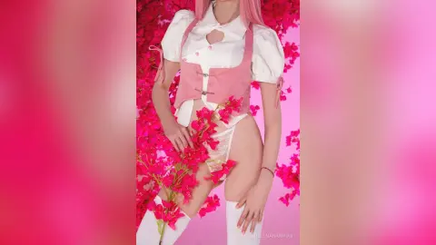 Woman in pink corset and white blouse posing with bright pink flowers in a dreamy aesthetic setting.