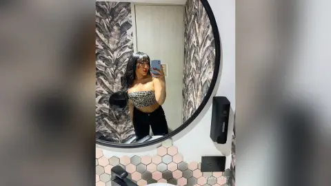 Young woman in a leopard print crop top taking a mirror selfie in a modern bathroom with tropical wallpaper.