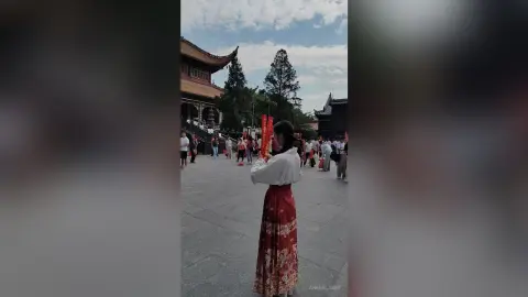Woman in traditional white and red Hanfu standing in a historic temple courtyard under a clear blue sky.