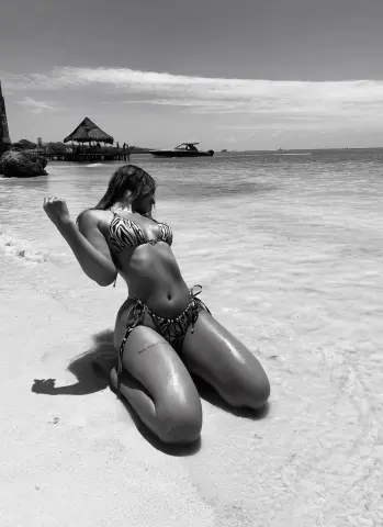 Young woman in patterned bikini relaxing on a sunny tropical beach with ocean waves in black and white.