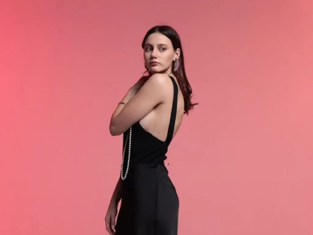 Young woman in a chic black backless dress posing against a vibrant pink background with a moody aesthetic.